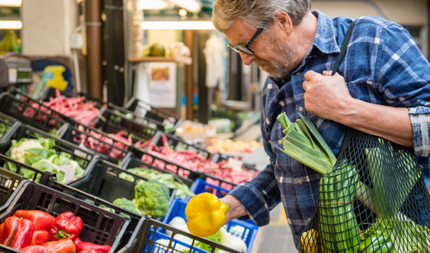 Older man with gray hair picking produce at grocery
